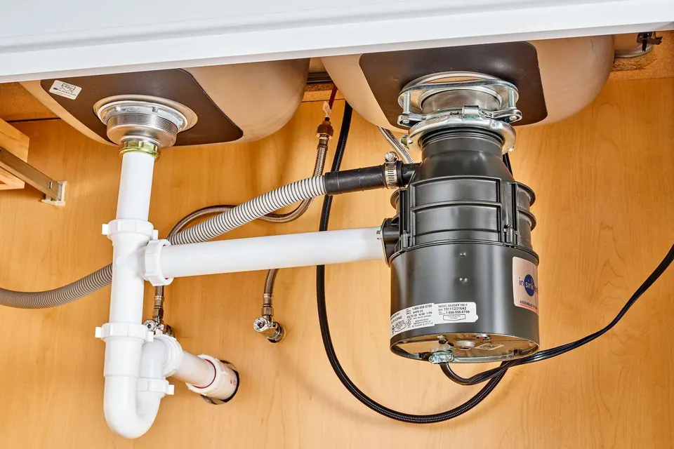Plumber checking a kitchen drain trap below a disposal